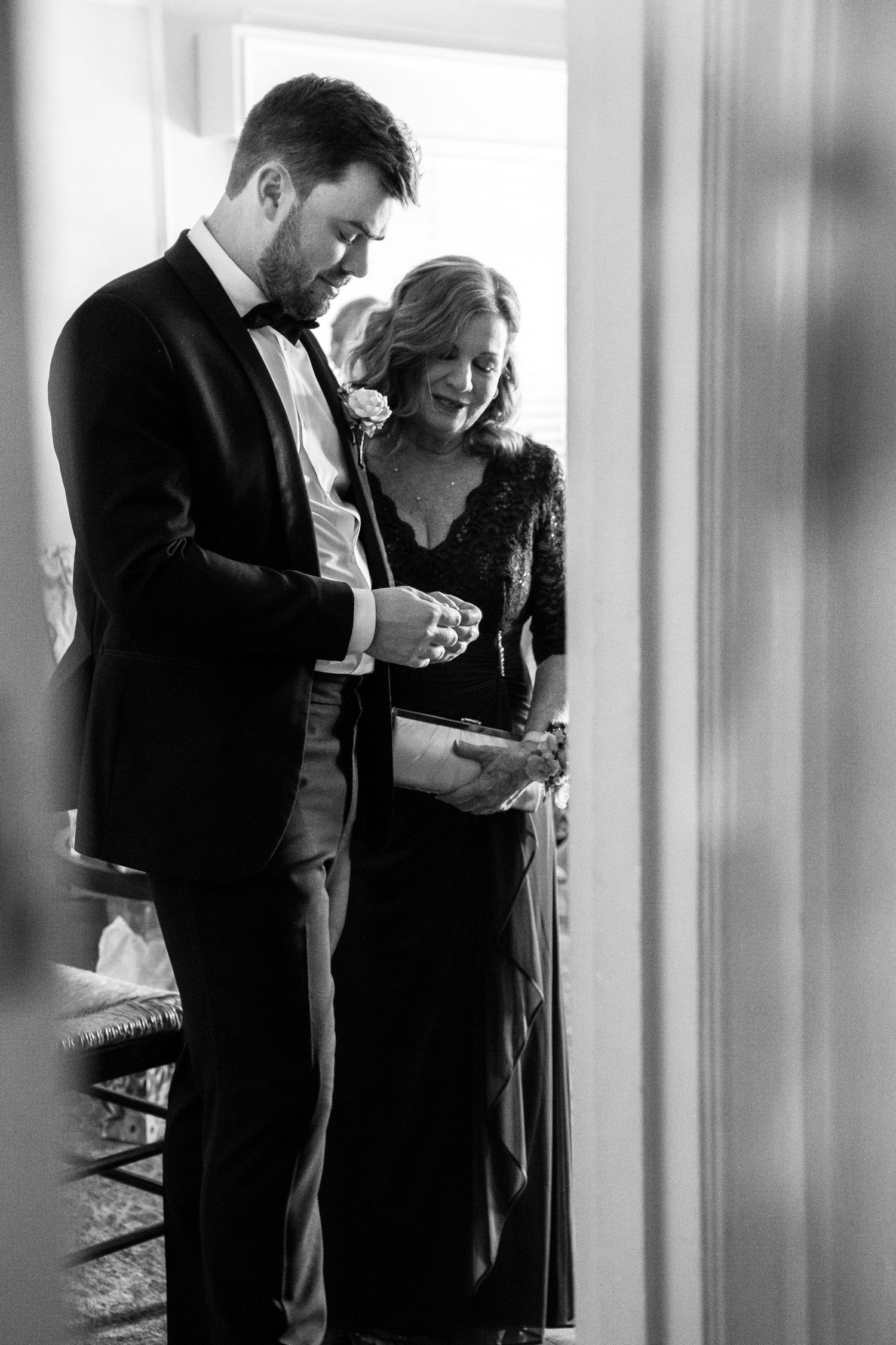 A couple in formal attire shares an intimate black and white moment against a light background.