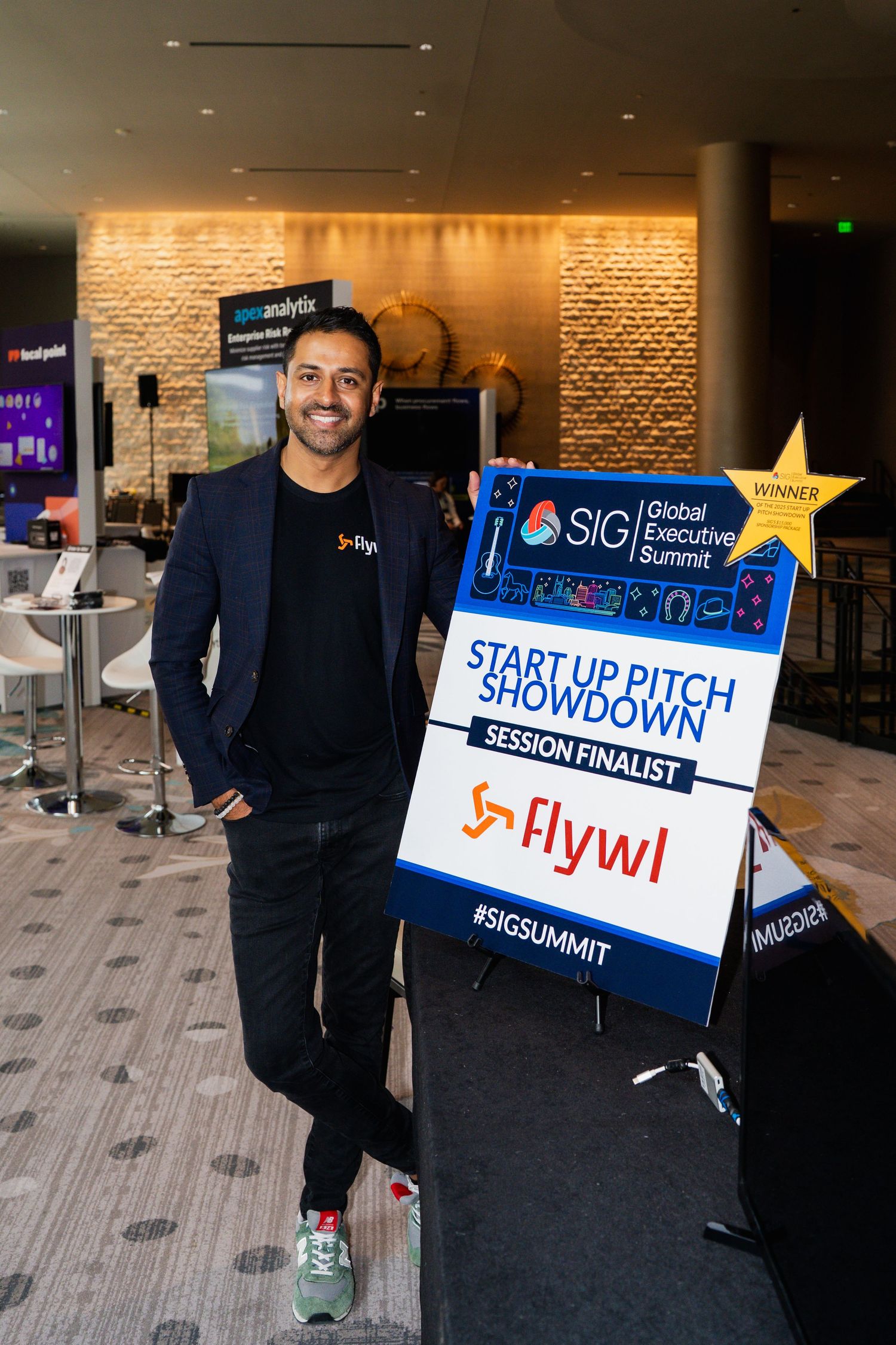 Man stands beside SIG Global Executive Summit Start Up Pitch Showdown Flywl finalist sign.