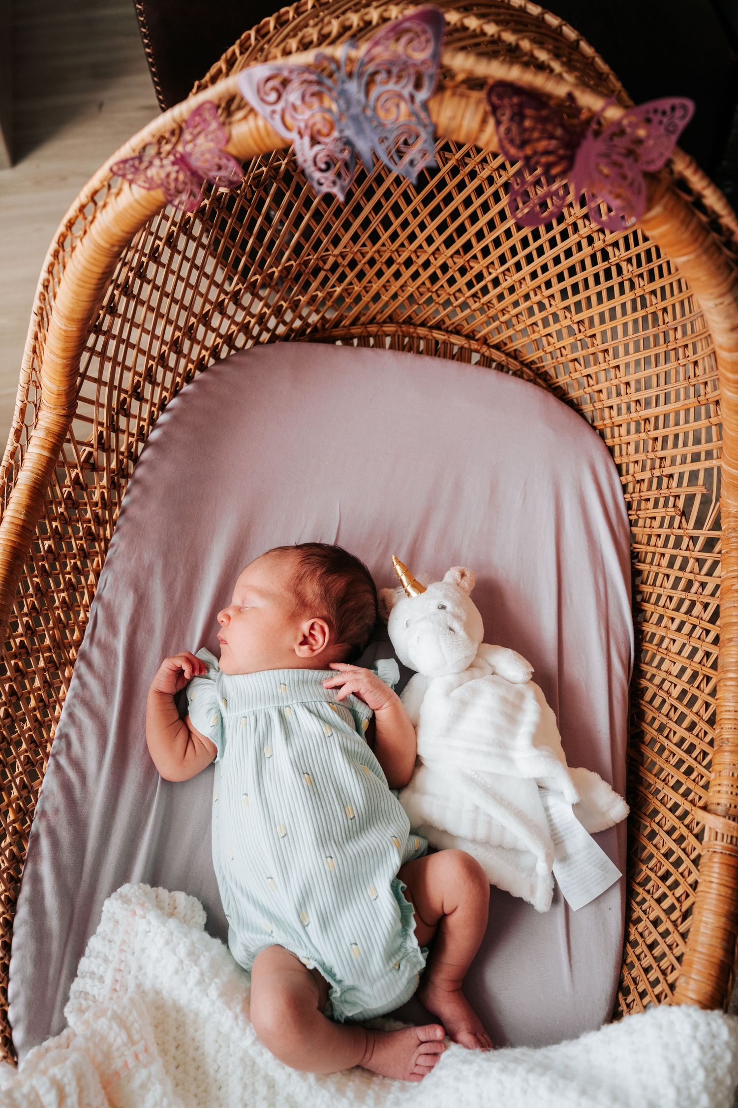 A series of photos showing a sleeping baby in a wicker chair with white and mint green clothing and blankets.