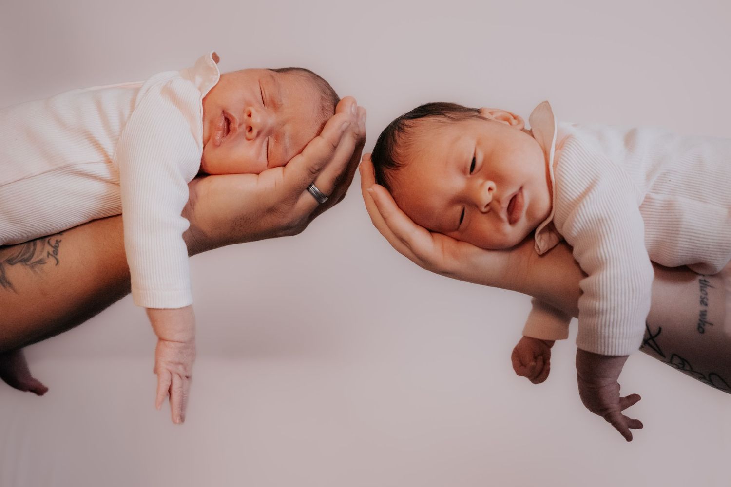 Two sleeping babies in white outfits lying on a white surface with hands cradling their heads.