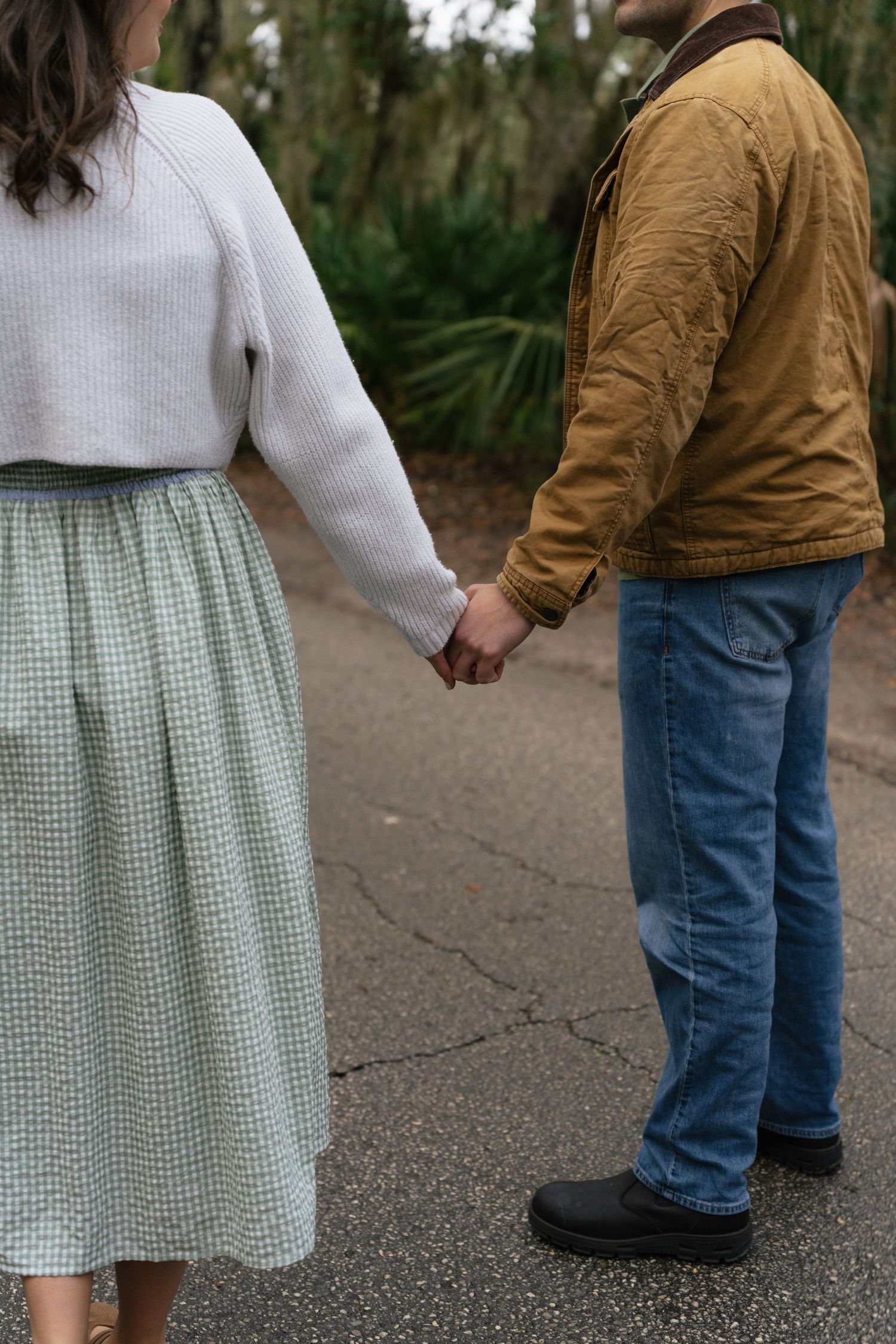 A couple holding hands while walking outdoors, wearing coordinated casual outfits with jeans and sweaters.