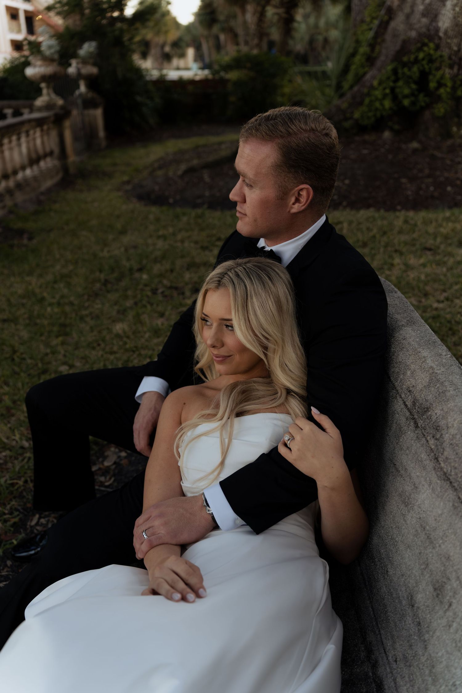 Romantic couple in wedding attire share intimate embraces while sitting together outdoors at dusk.