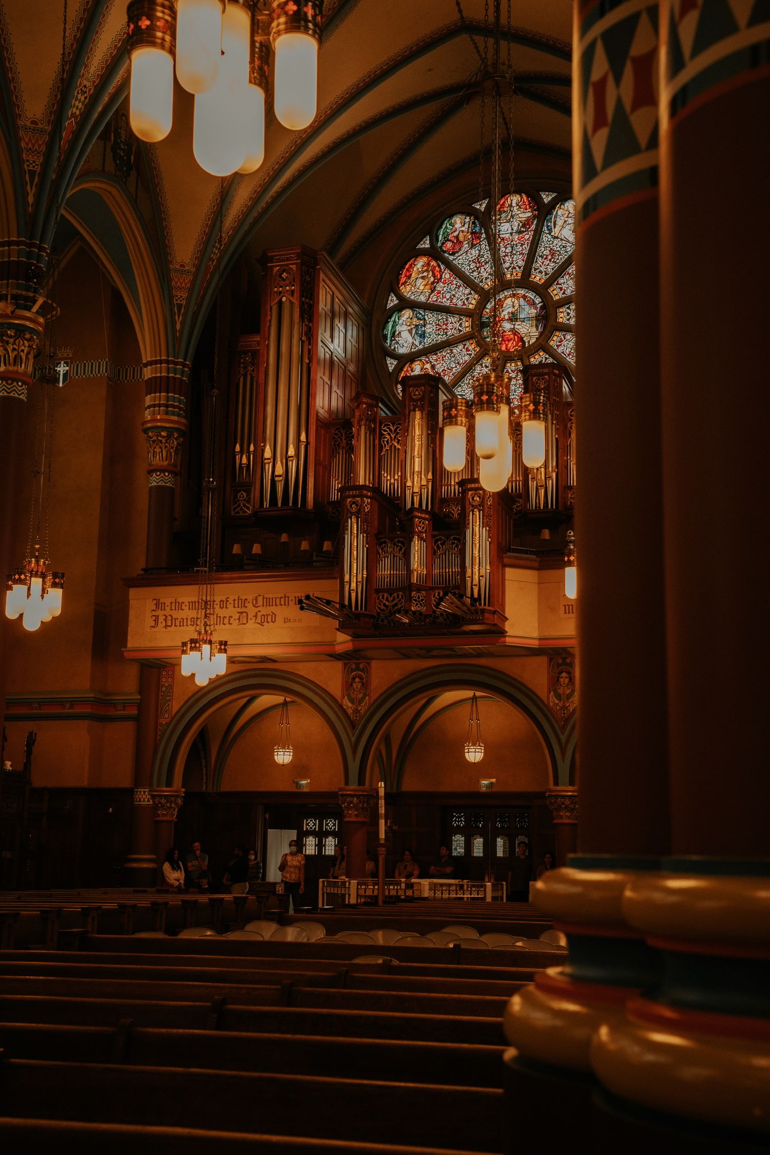 Gothic church interior with arched ceilings, wooden pews, and glowing pendant lights creating a warm ambiance.