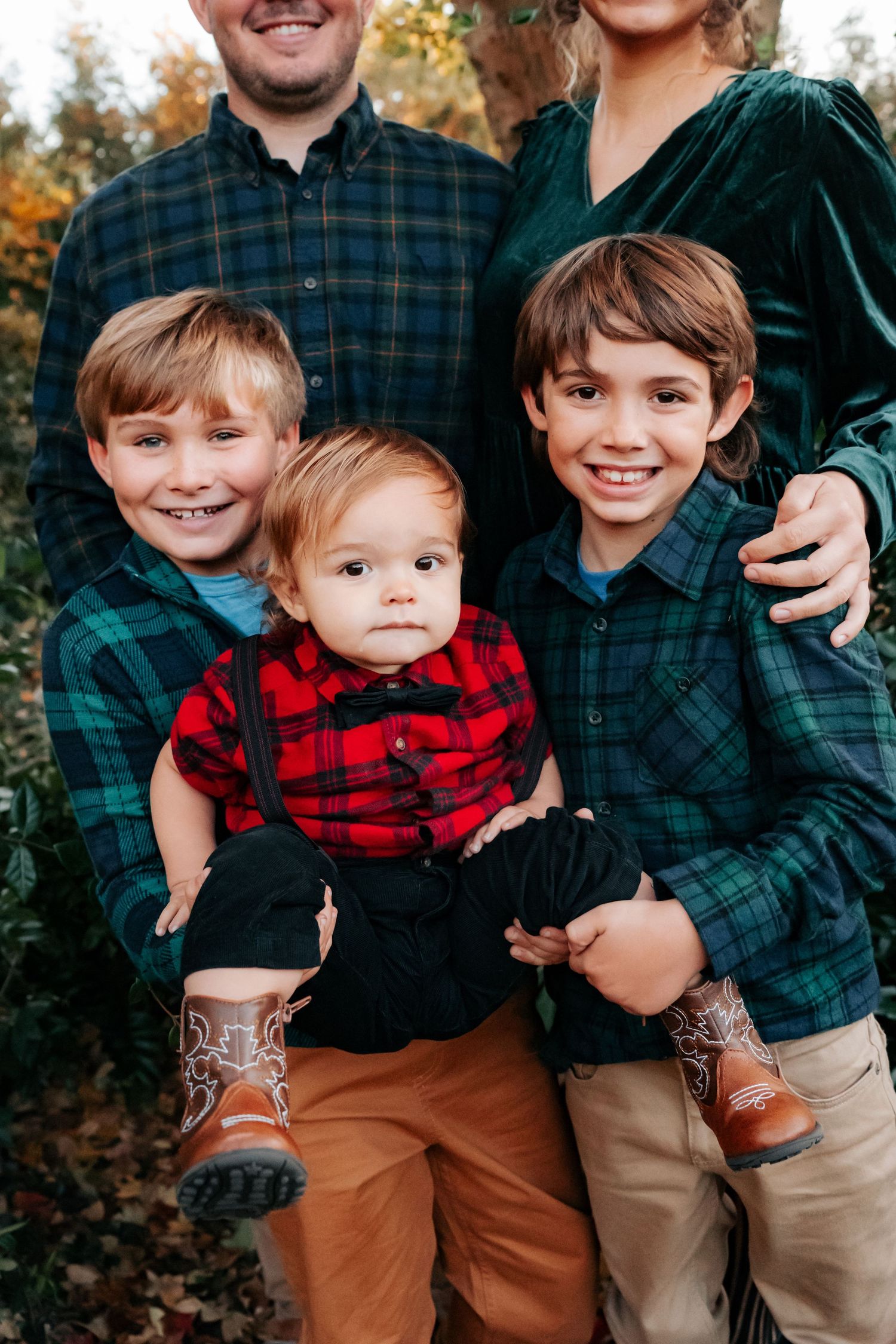 A family wearing coordinated buffalo plaid and flannel shirts poses together during an autumn outdoor photo session.