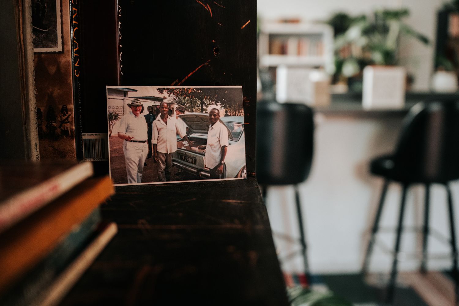 Vintage sepia photograph framed against a modern interior with bar stools and houseplants in the background.
