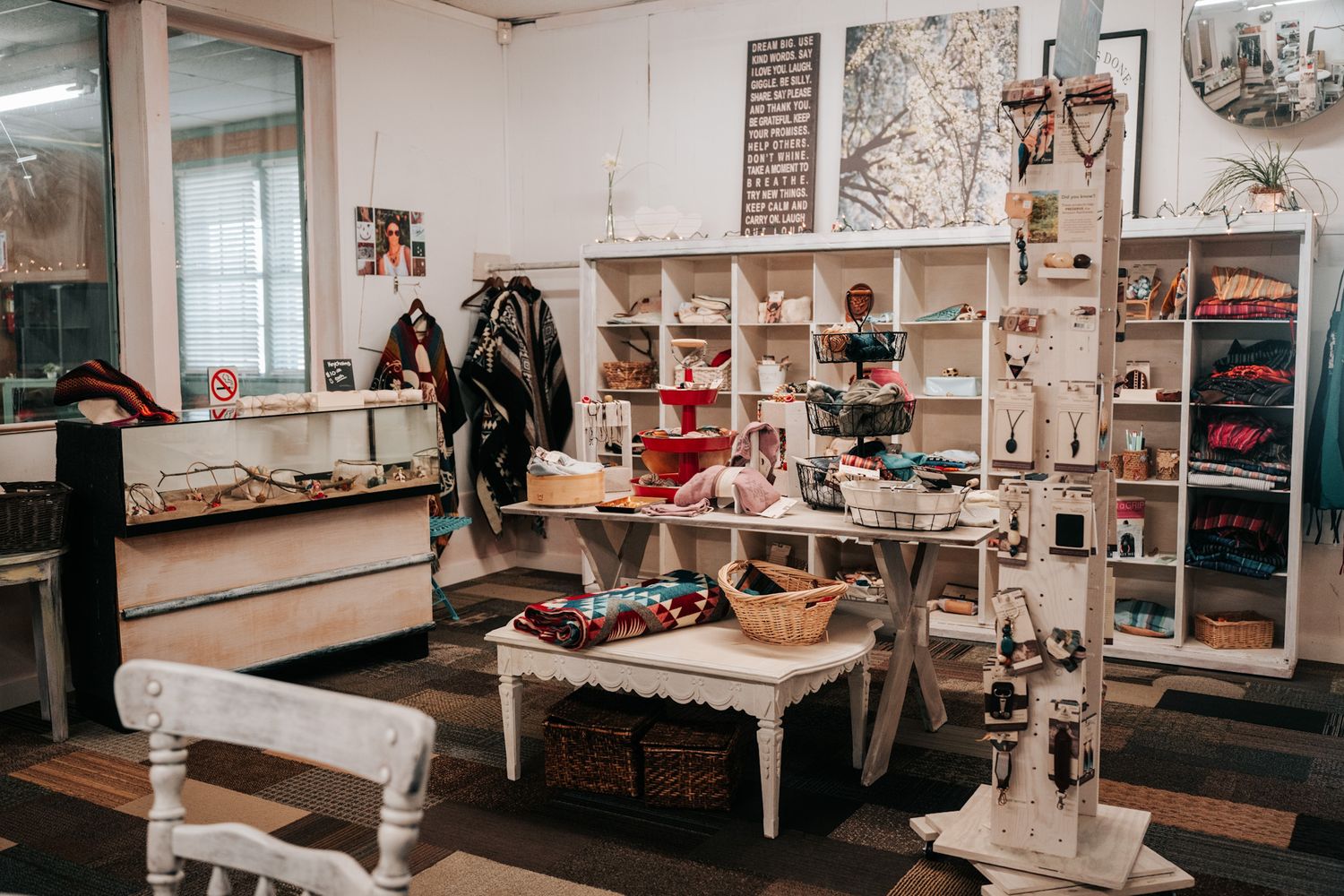 Interior view of a boutique store with white shelving units displaying clothing, accessories and home decor items.