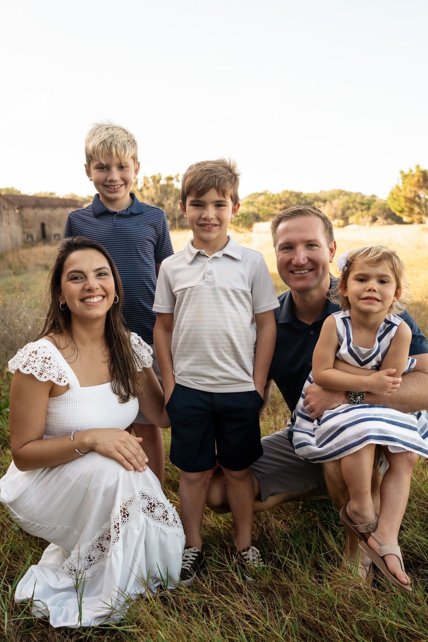 Family portrait in natural setting during golden hour with grass and trees in background.