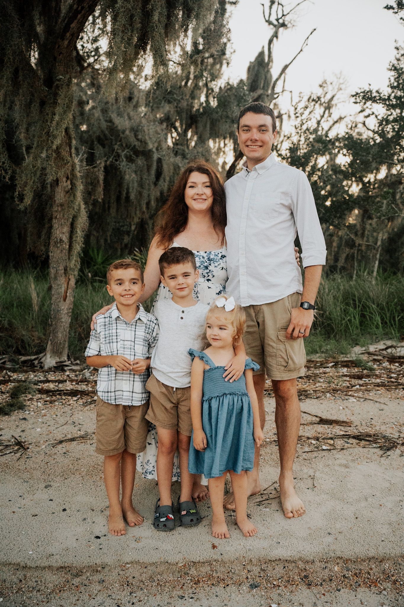 Family portrait outdoors with mossy trees, wearing coordinated casual summer outfits.