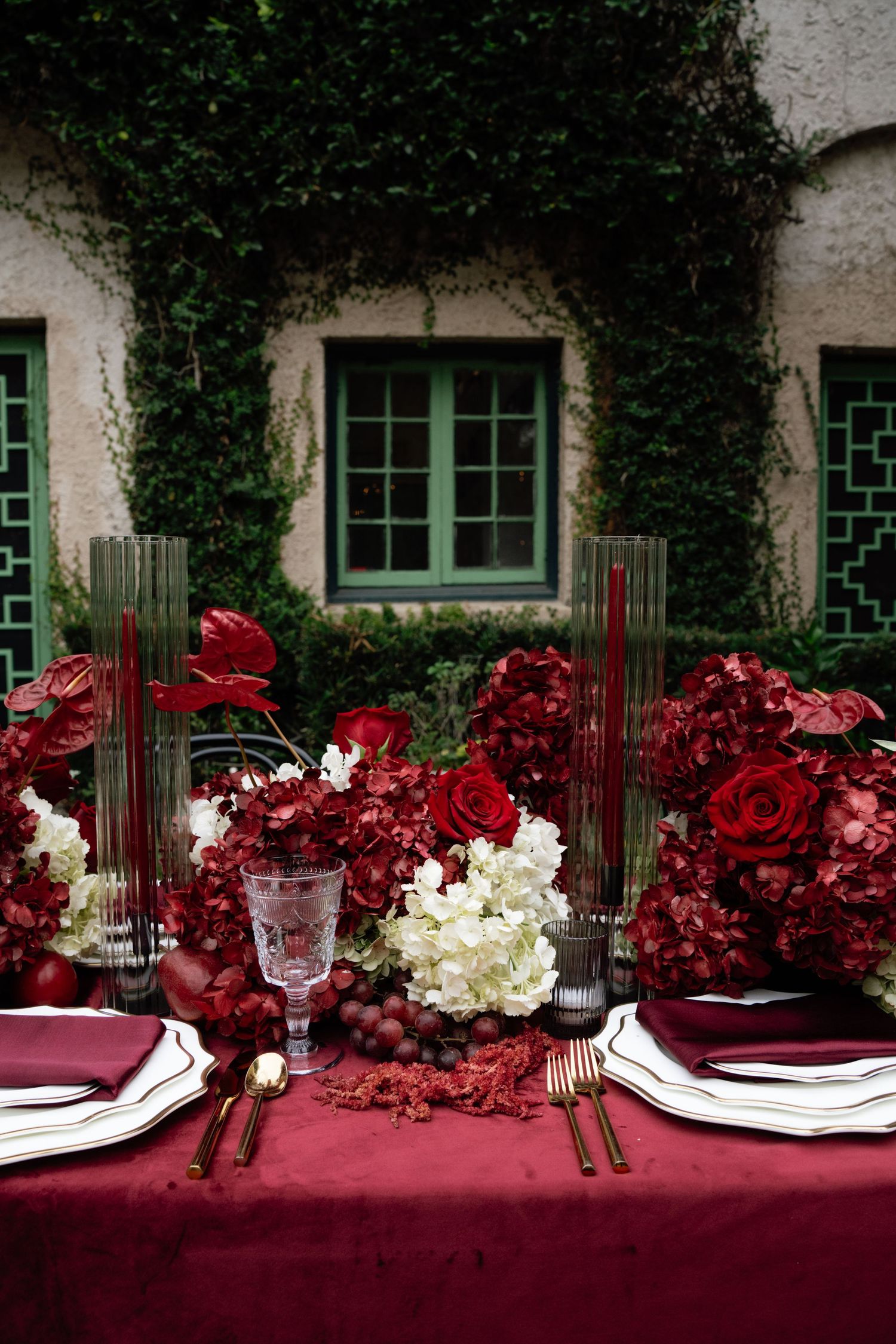 Elegant table setting with burgundy tablecloth, white plates, crystal glasses and deep red floral arrangements.