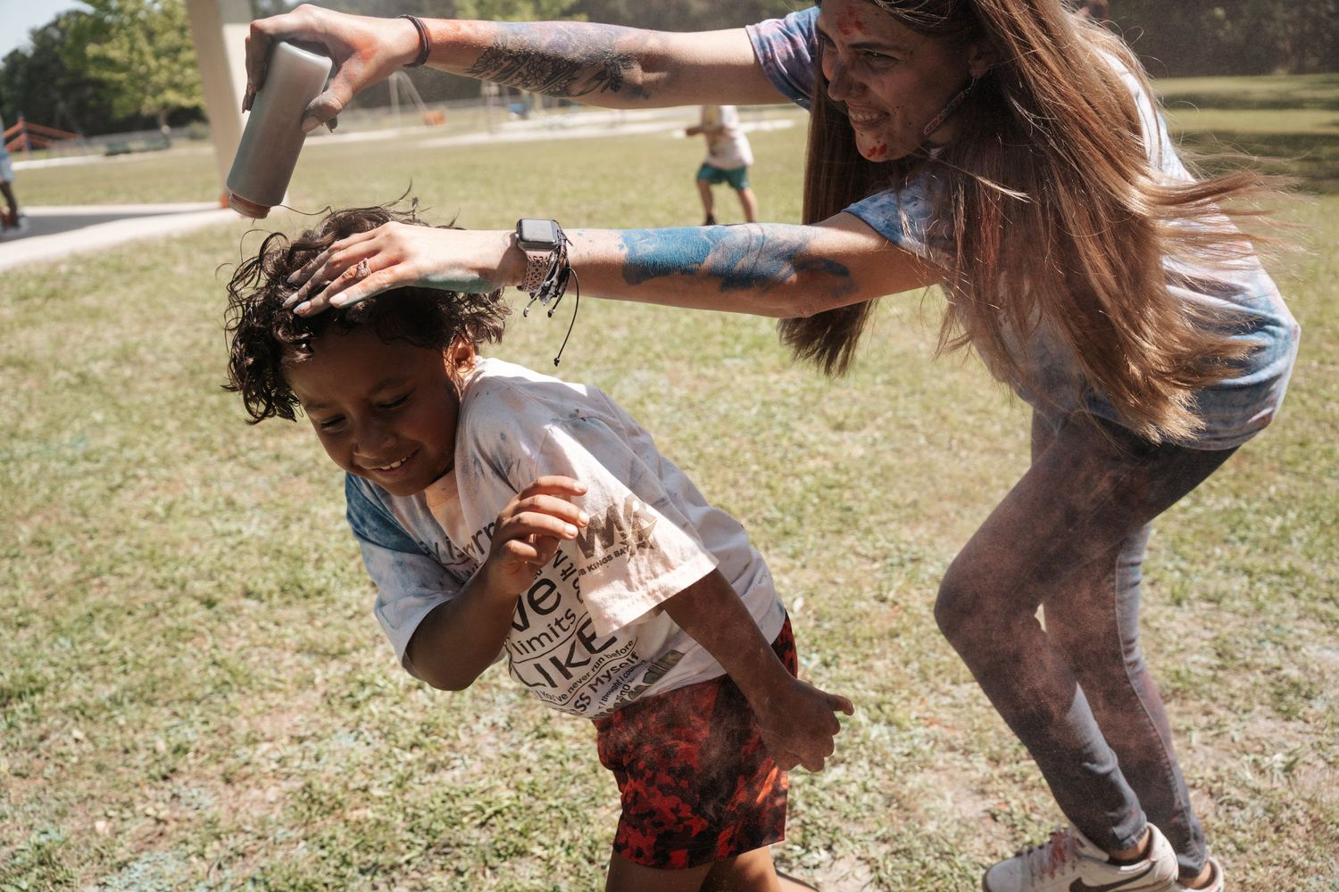 Two girls playing at a color run event outdoors, covered in colorful powder on a sunny day.