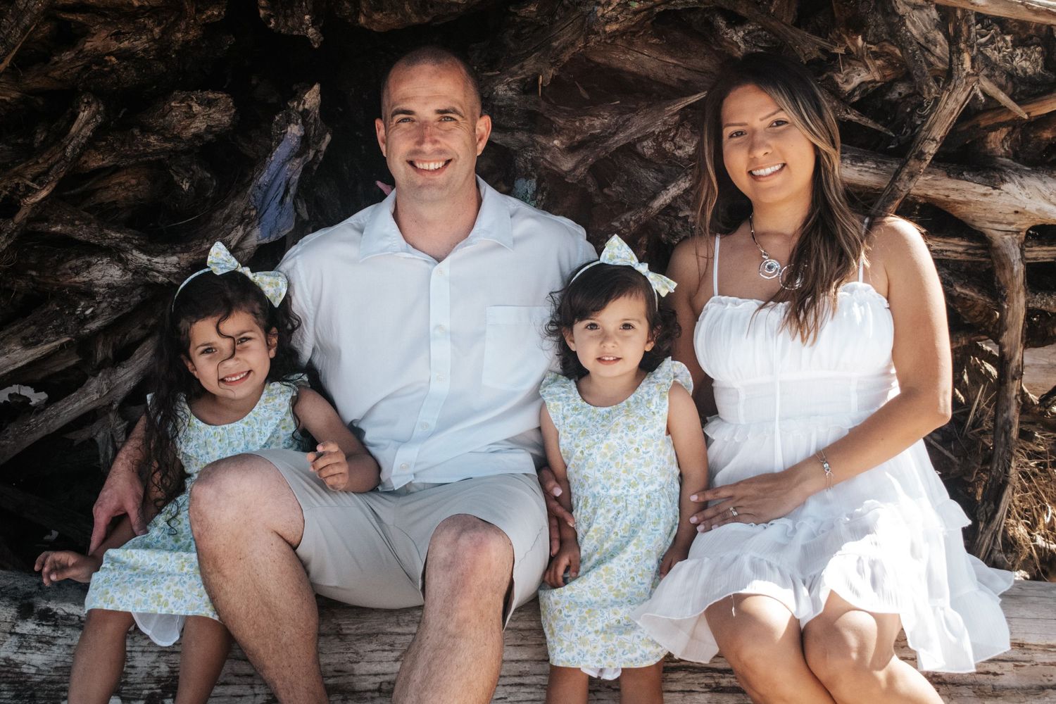 Family dressed in white poses together under a rocky overhang at the beach.