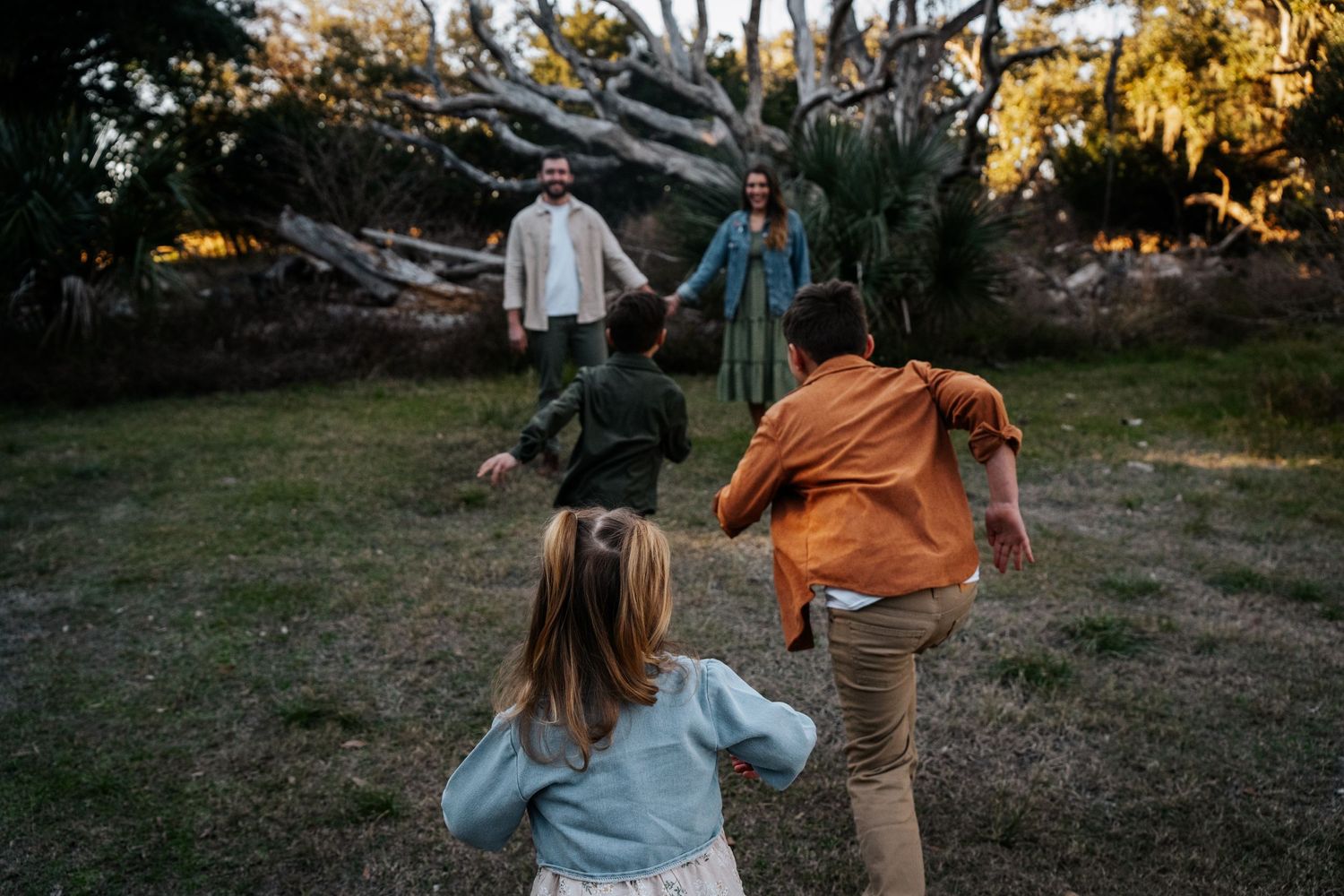 Family playing together in a backyard at dusk with dramatic tree backdrop.