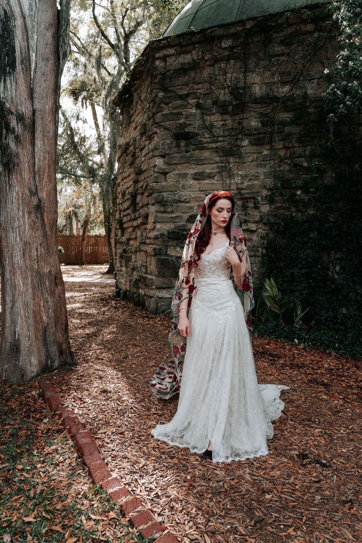 Bridal portrait in romantic garden setting with stone wall, brick path and flowing lace wedding gown.