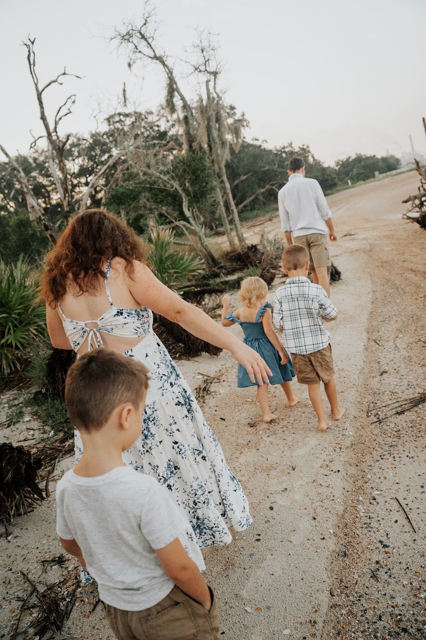 Family walking together on sandy trail with mossy trees and driftwood in background.