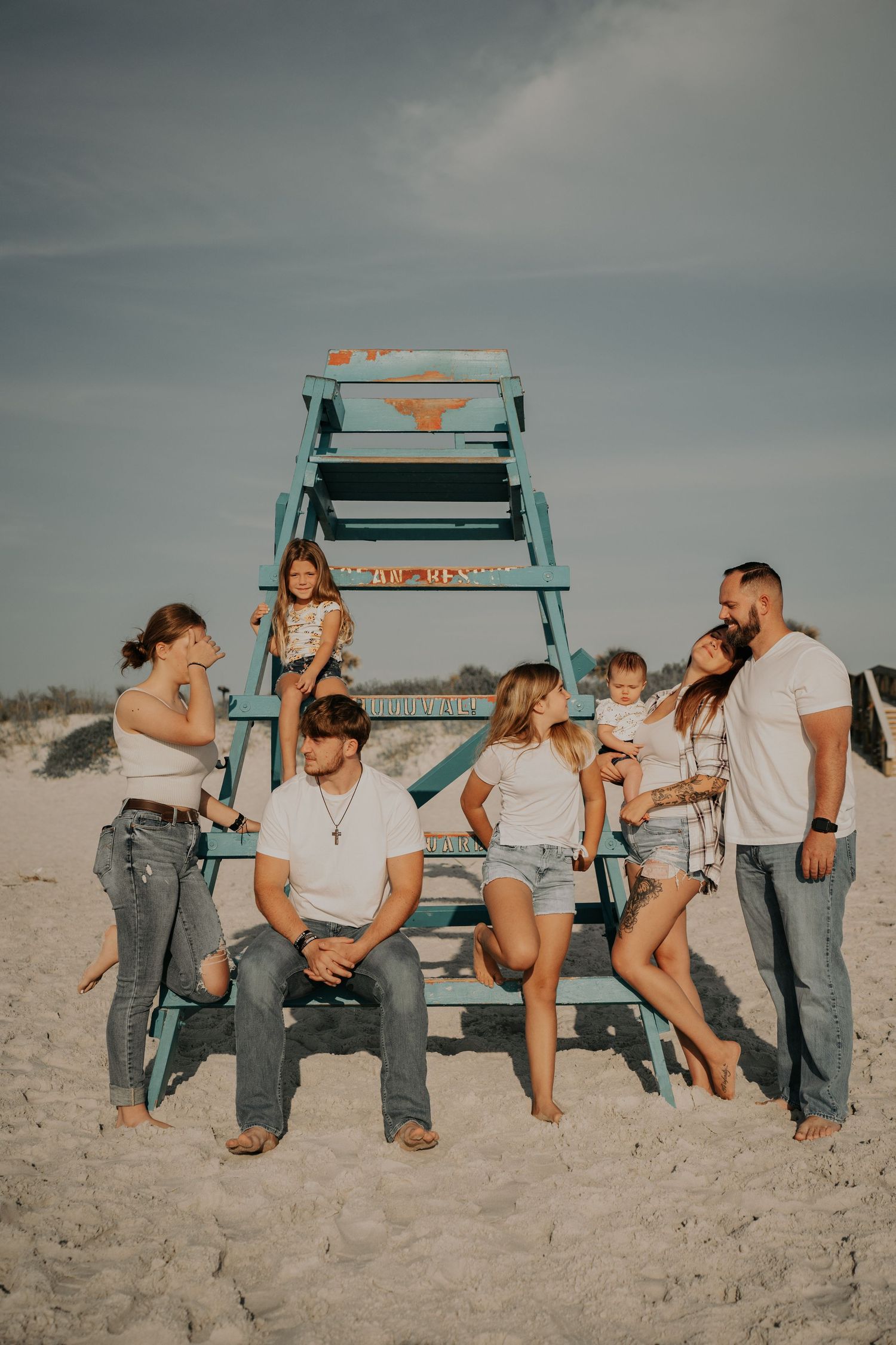 Group poses on beach against blue lifeguard tower during cloudy day.