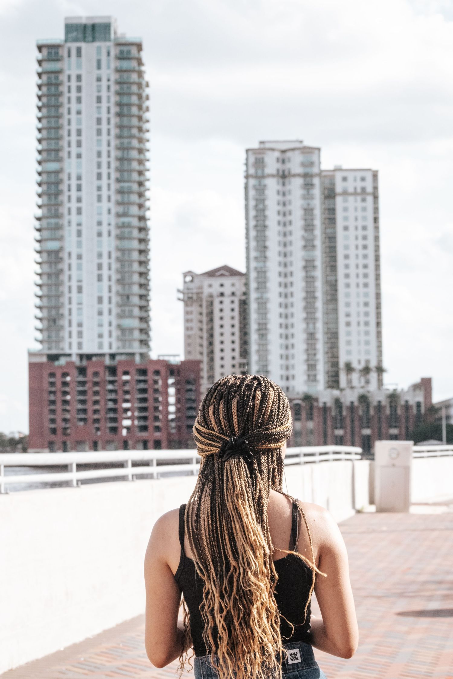 Person with braided hair looks out at urban skyline with modern high-rise buildings in the background.
