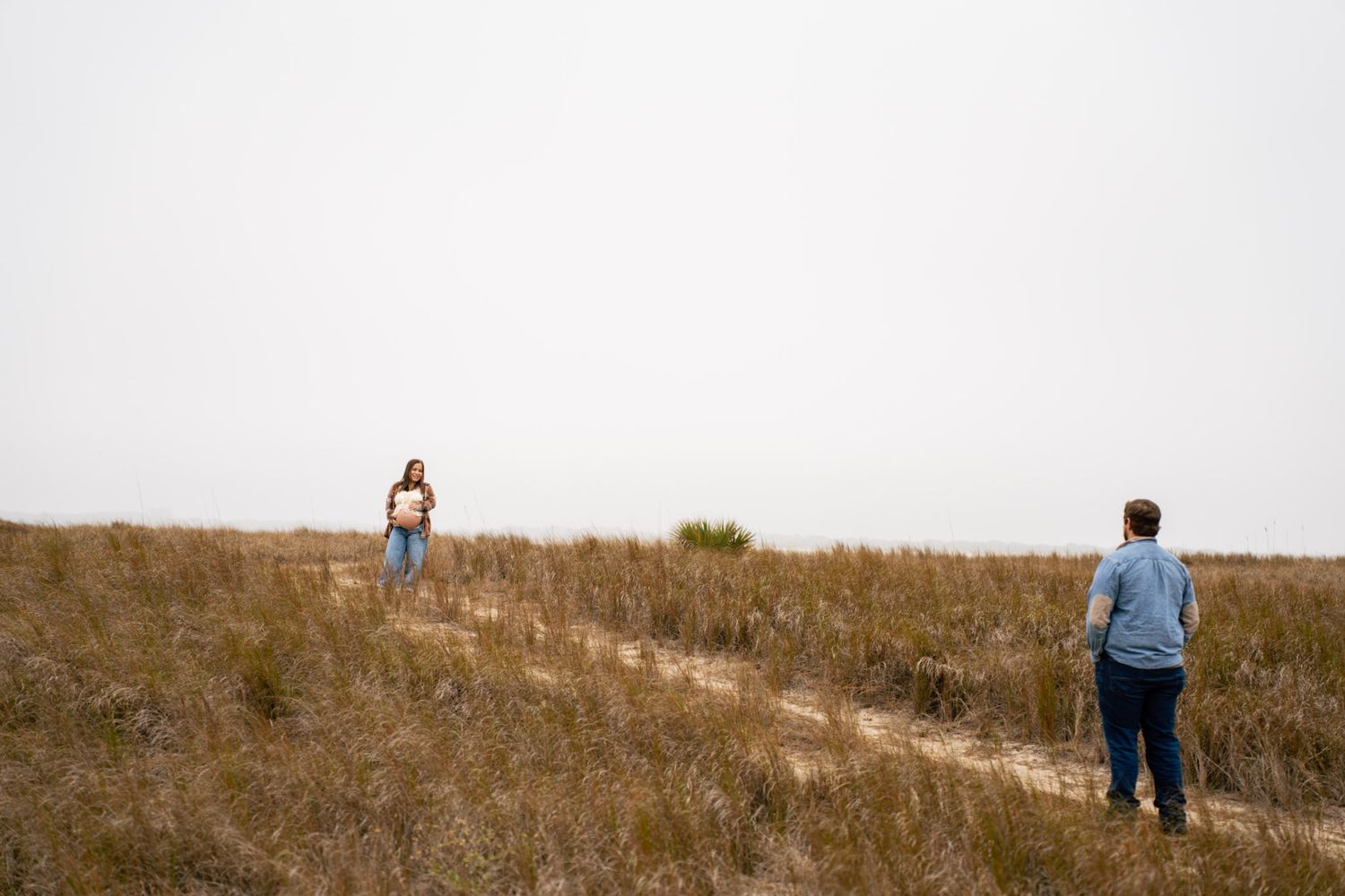 Person standing on a grassy hillside slope against a bright sky during daytime.