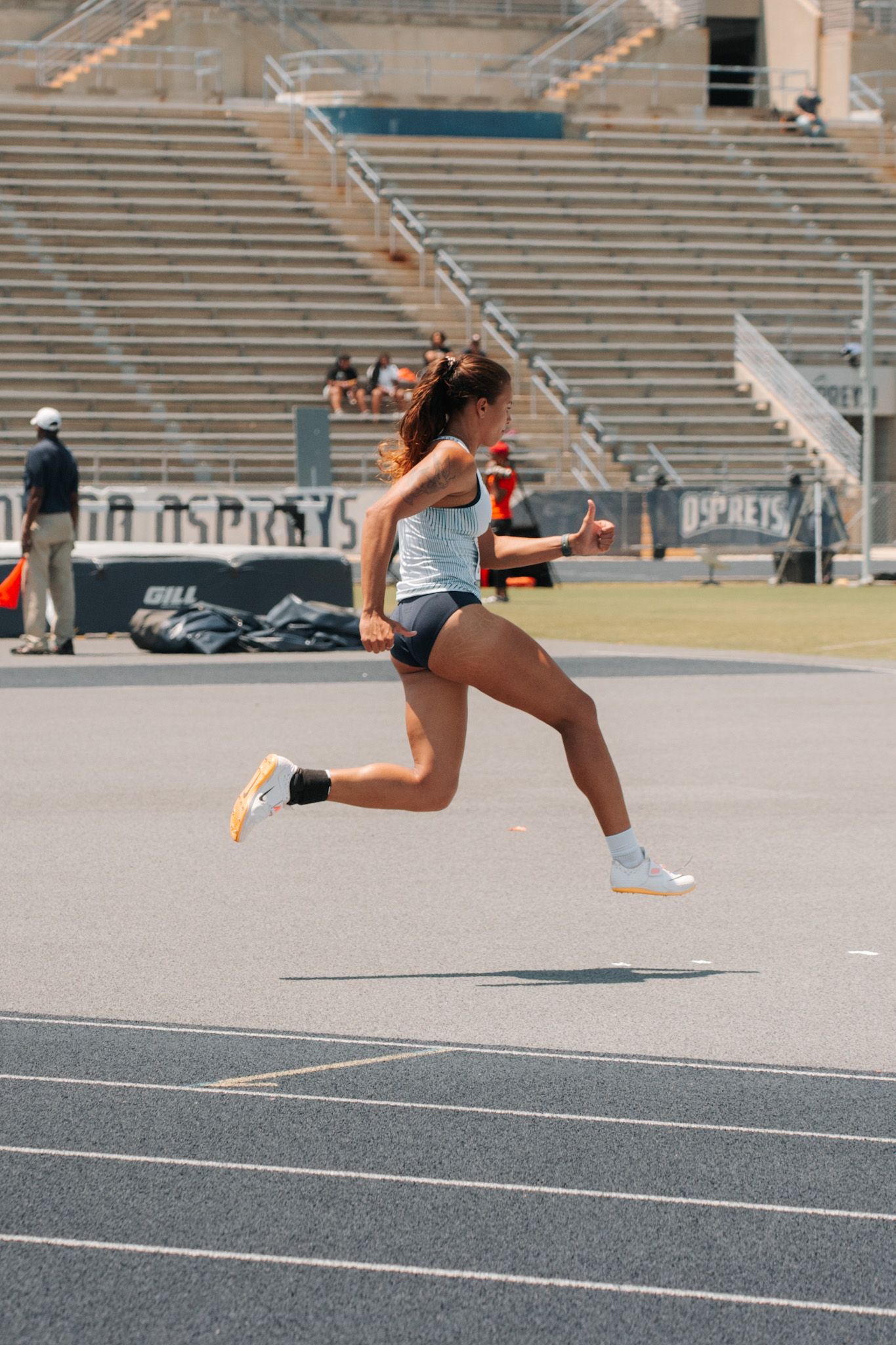 Female athlete sprinting on a track during a competition at a stadium with bleachers in the background.