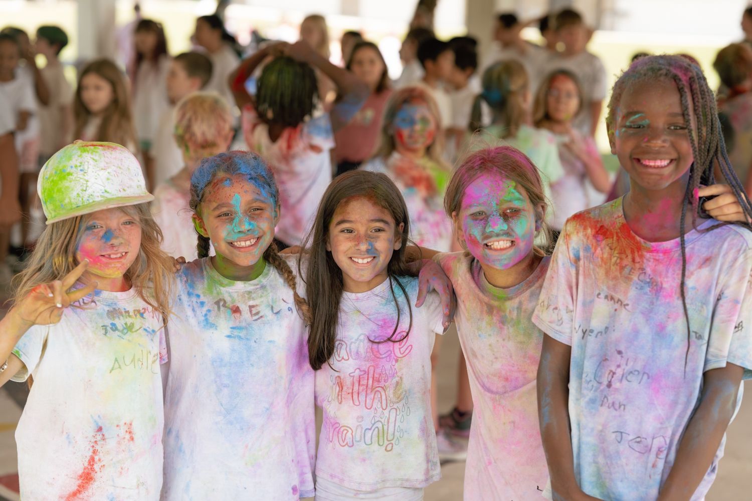 Five girls covered in colorful Holi powder smile together at a festive color run event.
