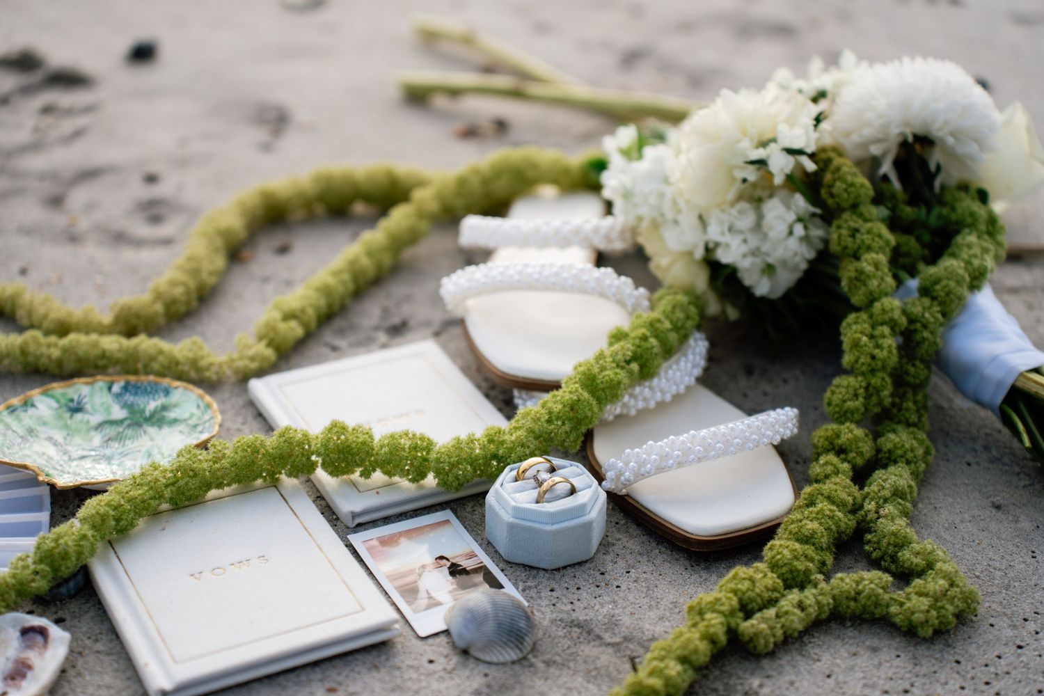Wedding decor elements with moss garland, white floral arrangements, and delicate ceramic details on a textured surface.