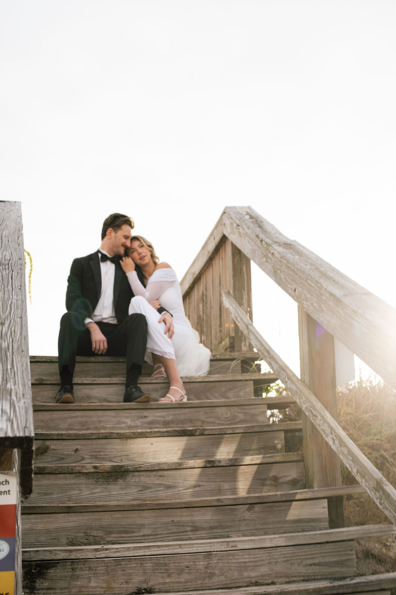 A couple in wedding attire shares romantic moments on rustic wooden stairs during a sunset photo session.