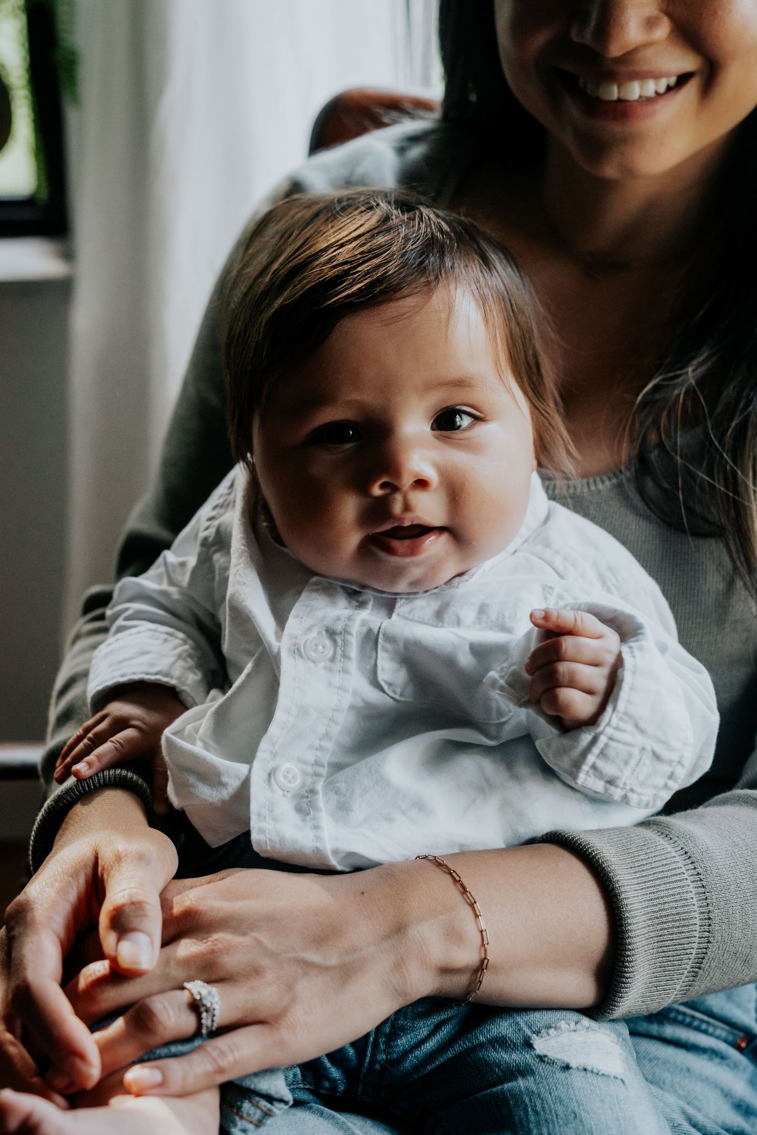 A baby wearing a white ruffled collar smiles while being held in someone's lap.