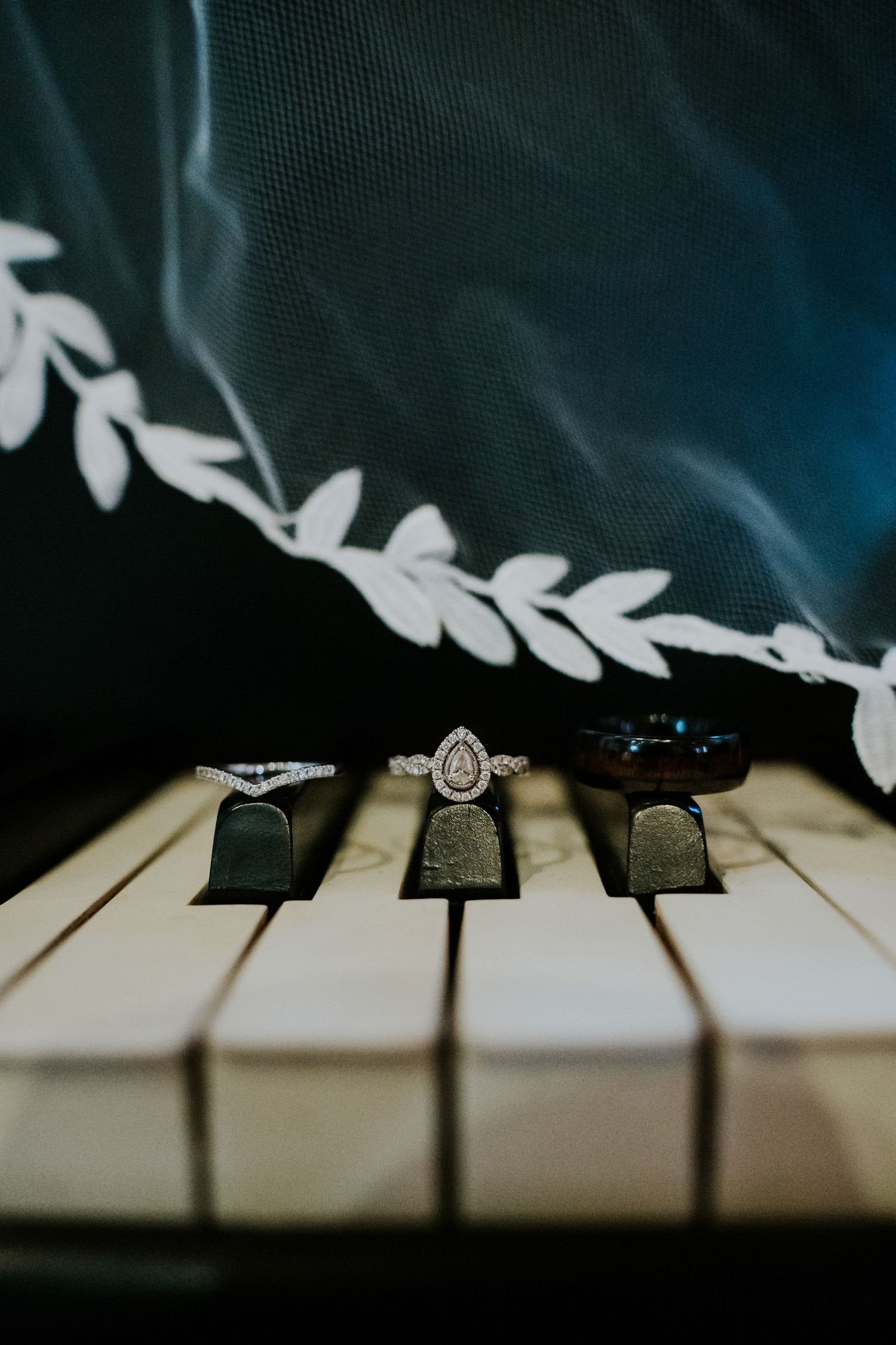 A diamond engagement ring rests elegantly on black and white piano keys in dramatic lighting.