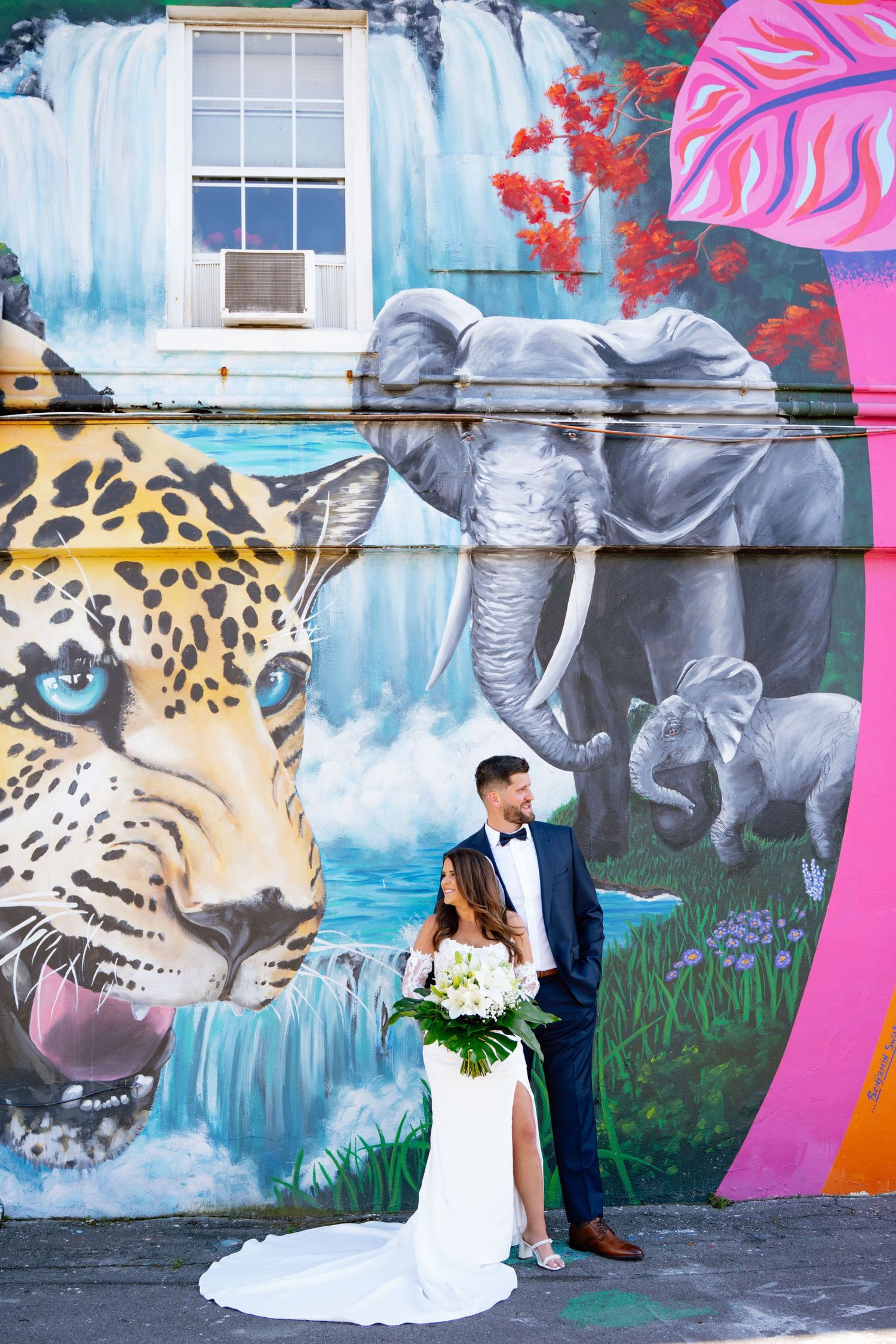 Bride and groom pose in front of vibrant wildlife mural featuring elephant and leopard on wedding day.