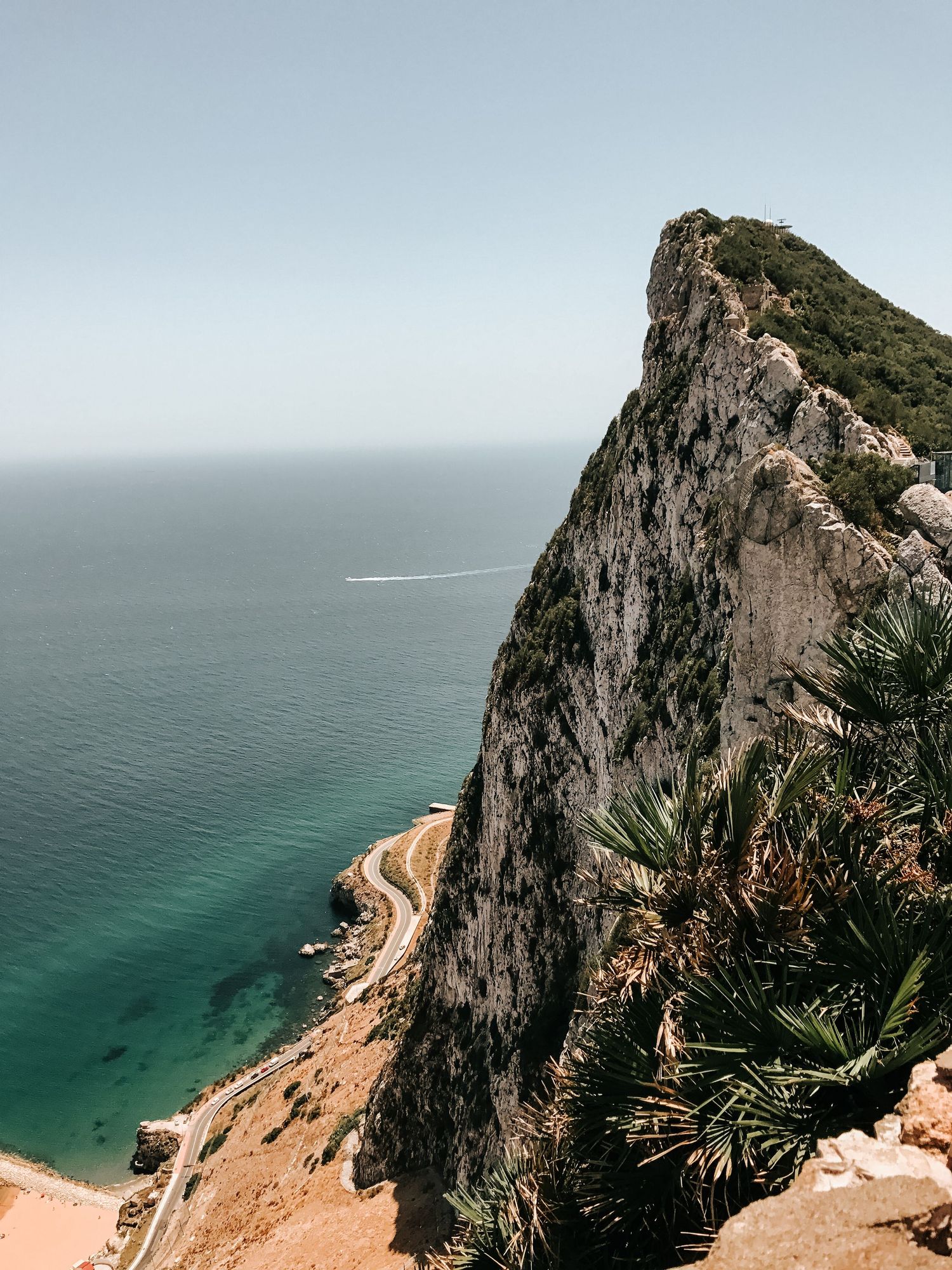 Dramatic aerial view of a steep coastal cliff overlooking turquoise waters and a winding coastal road in Gibraltar.