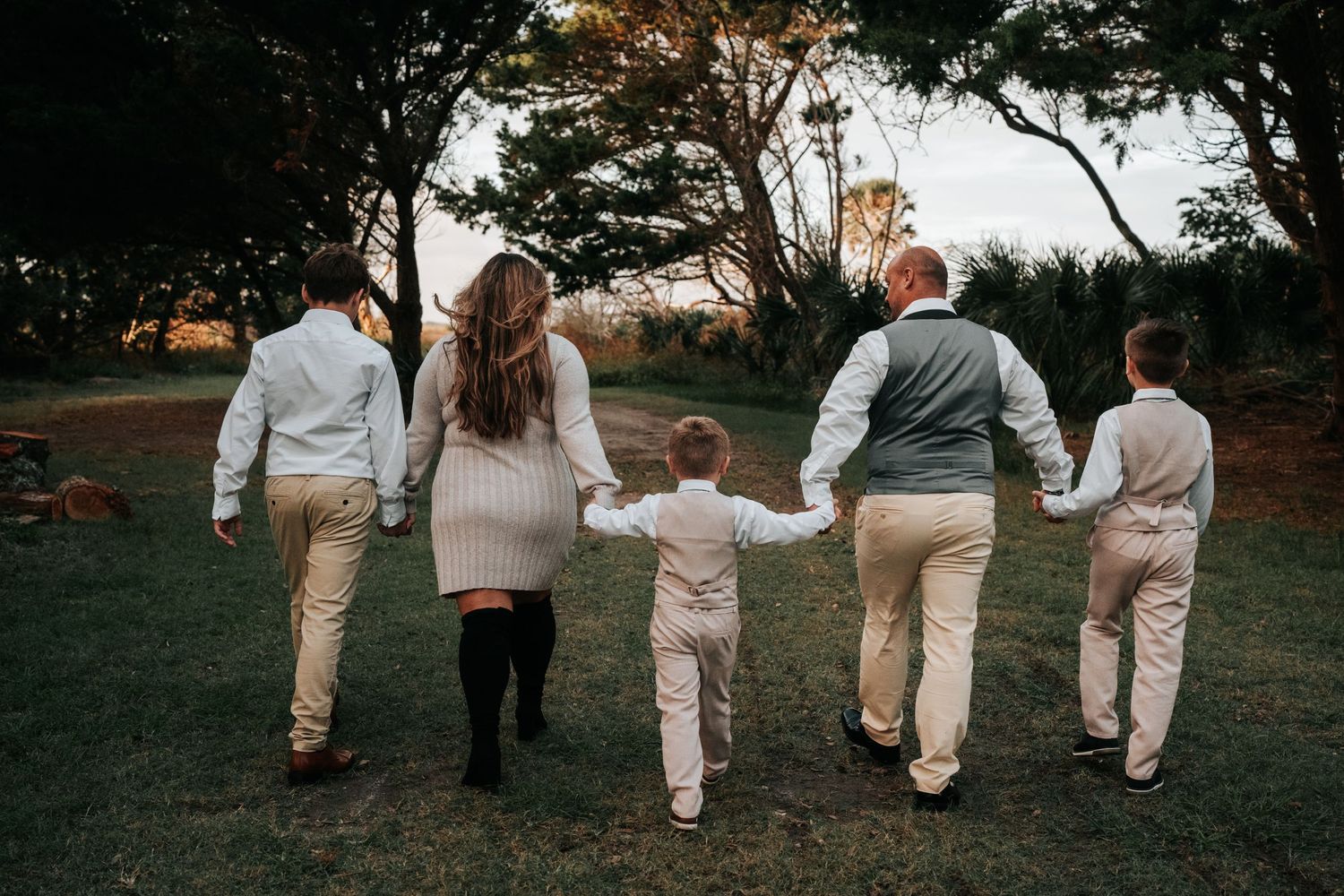 Family holding hands while walking through a grassy area in coordinated cream colored outfits.