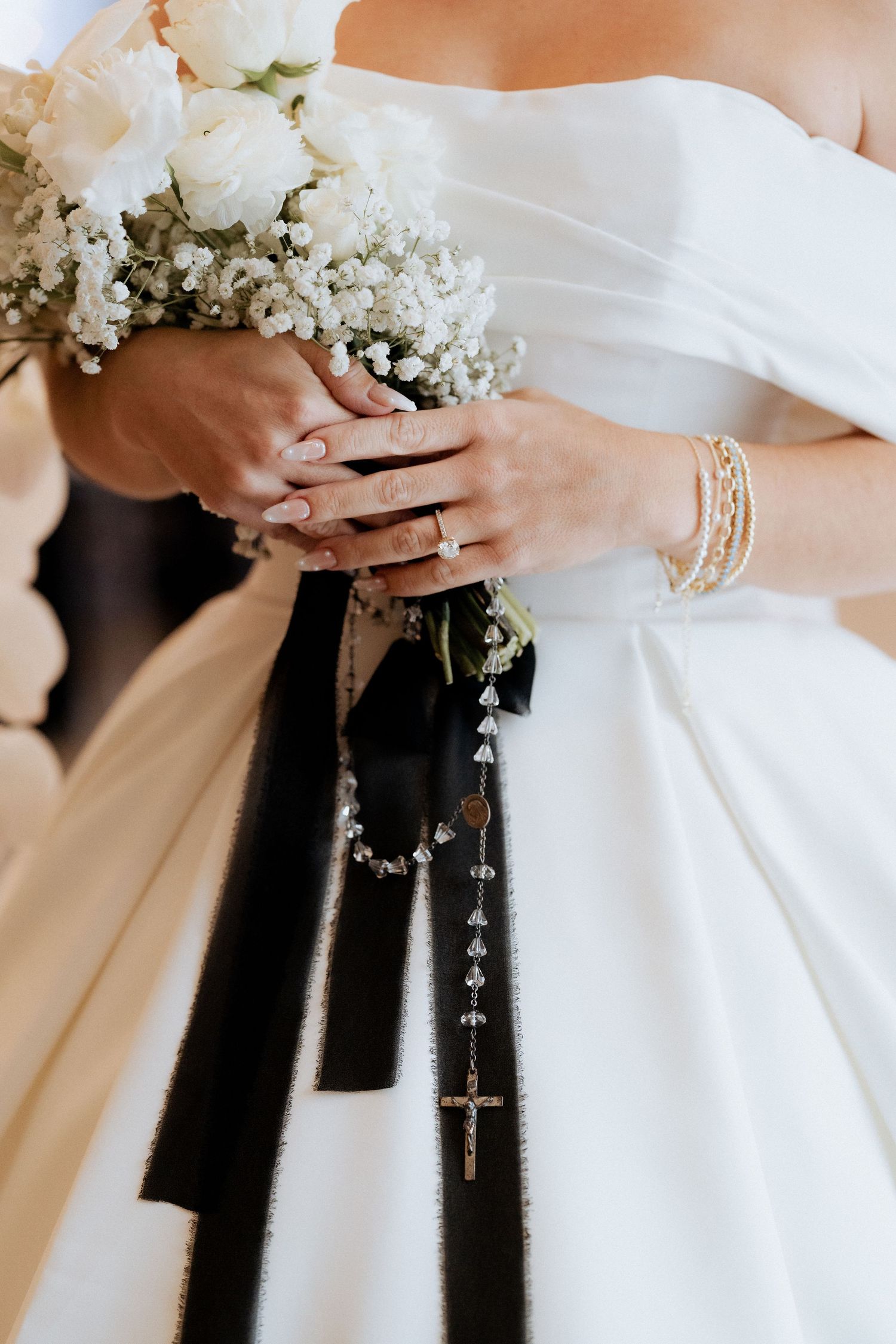 Close-up view of white bridal bouquet held against black and white formal wedding attire with delicate floral details.