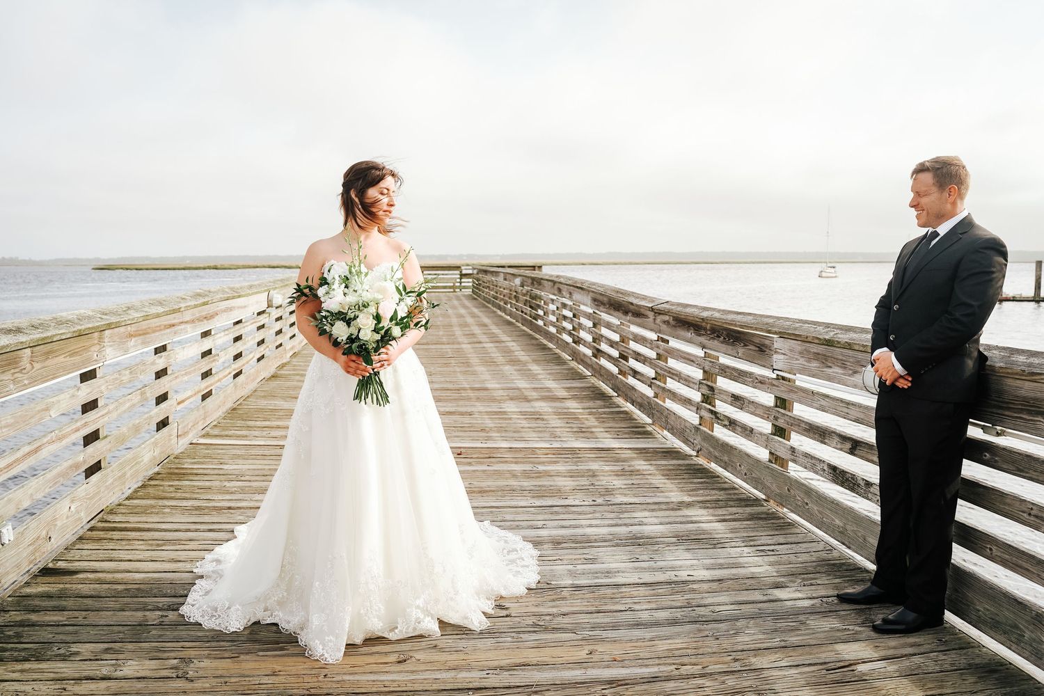 Romantic wedding couple poses on a wooden boardwalk overlooking the beach at sunset.