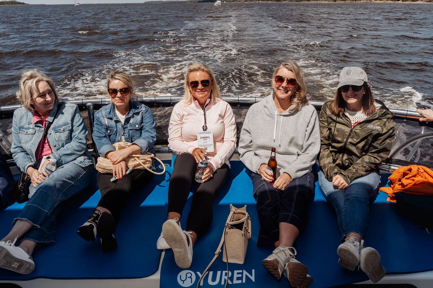 Five women sitting on a blue Yuren boat on the water, smiling on a sunny day.