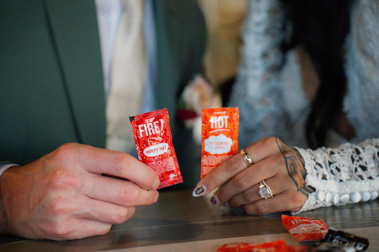 Two red and white Enjoy Life Foods snack containers sit on a dark wooden surface while hands reach for them.