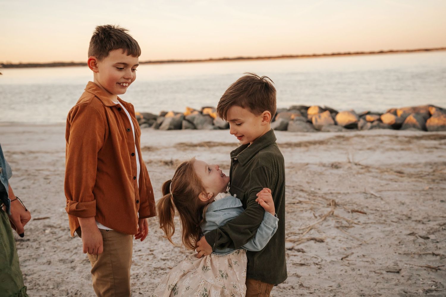 Three children playing and laughing together on a beach at sunset.