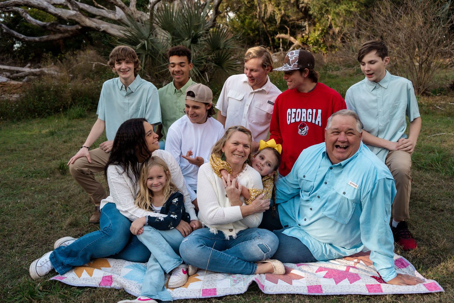 Multi-generational family gathered outdoors for a casual portrait on a blanket in a garden setting.