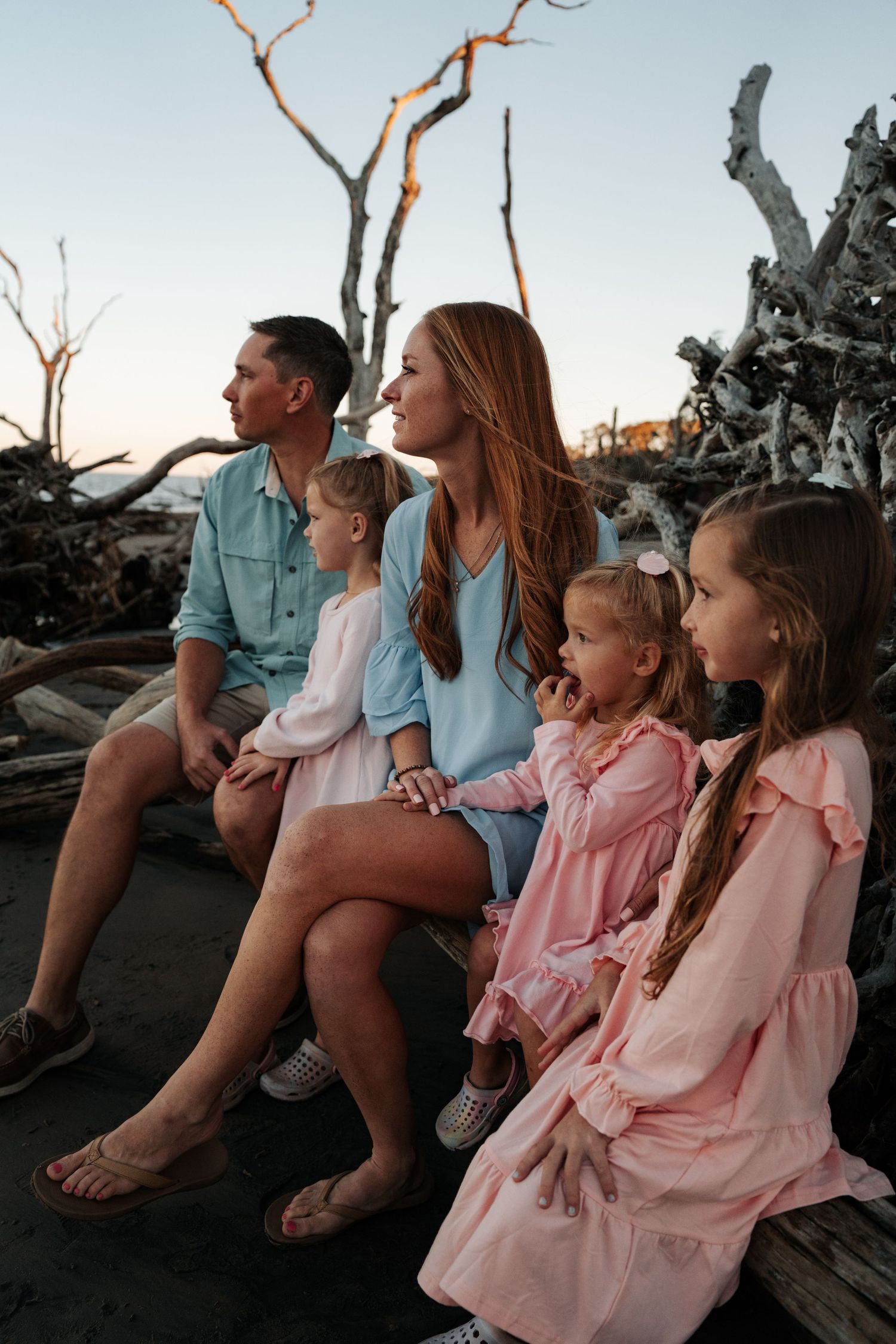 Family sitting together on driftwood at beach during sunset.