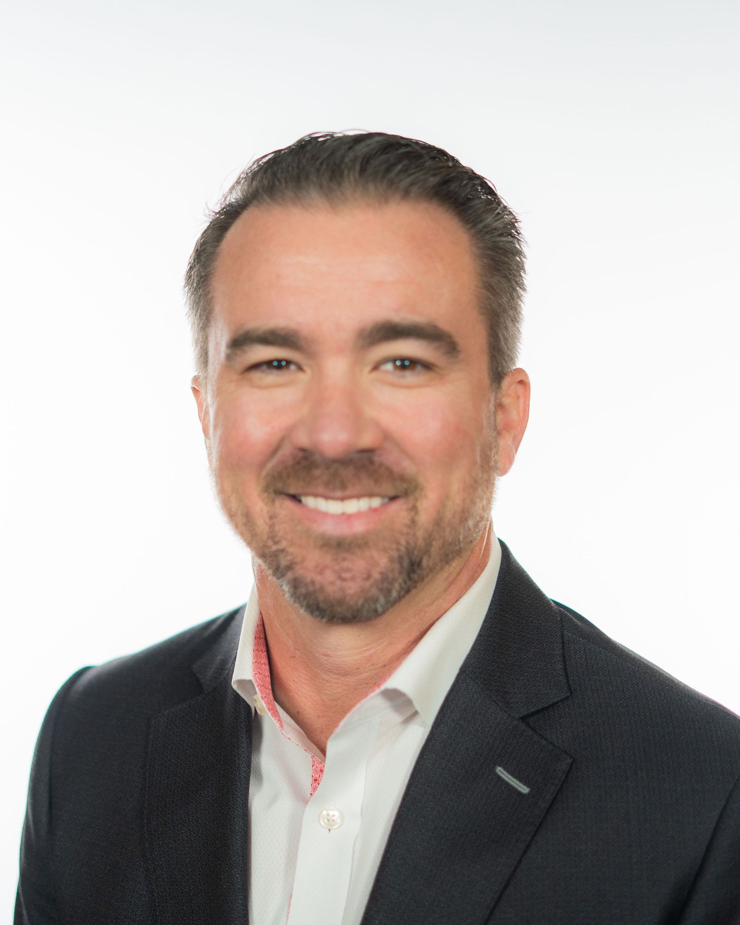 Professional headshot of a smiling middle-aged man with dark hair and beard wearing a navy blazer and white shirt.