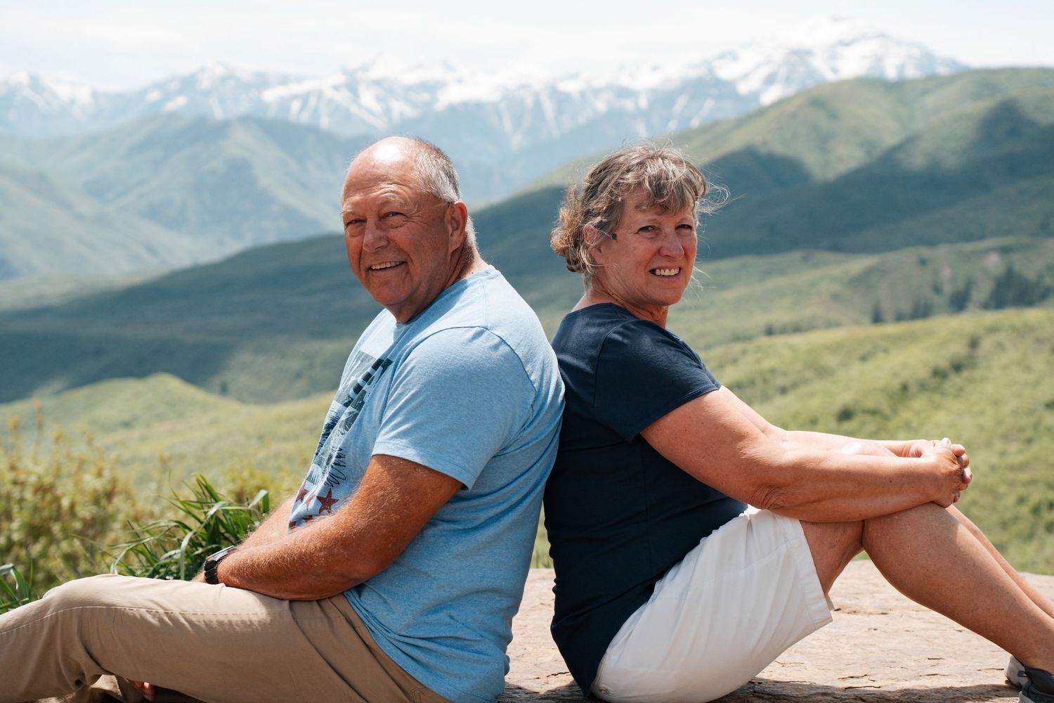 Two people sitting on a bench enjoying scenic mountain views on a sunny day in an outdoor setting.