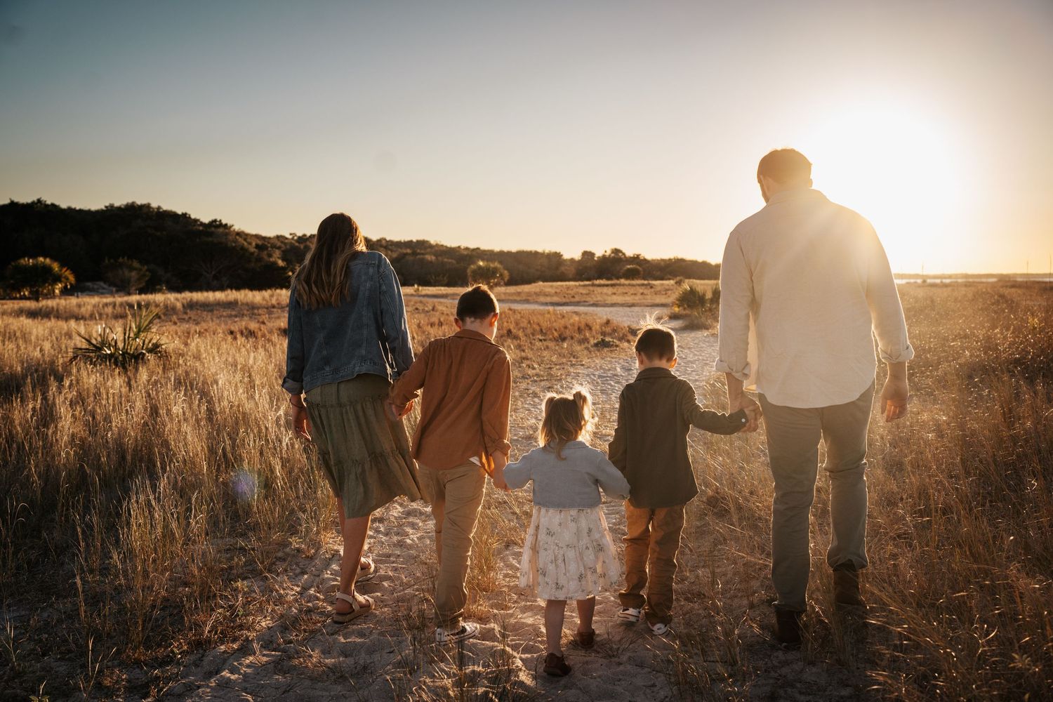 A family walks together through a golden field at sunset, silhouetted against the warm glowing sky at Fort Clinch
