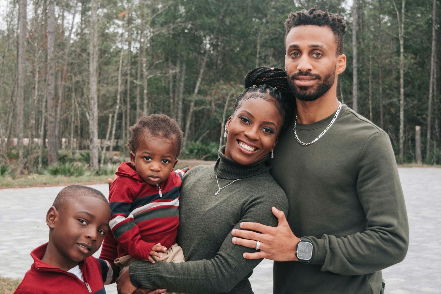 A family of four poses together outdoors on a winter day in front of a wooded forest background.