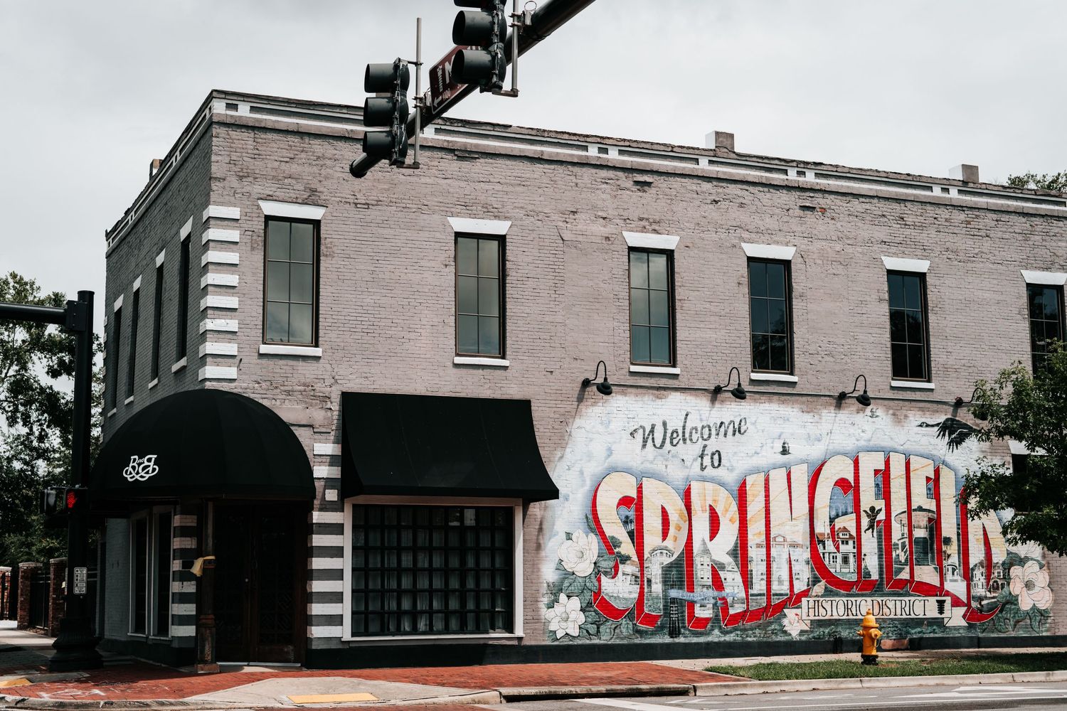 Historic brick building with colorful 'Welcome to Springfield' mural painted on its exterior wall and vintage street light. Brick and Beam