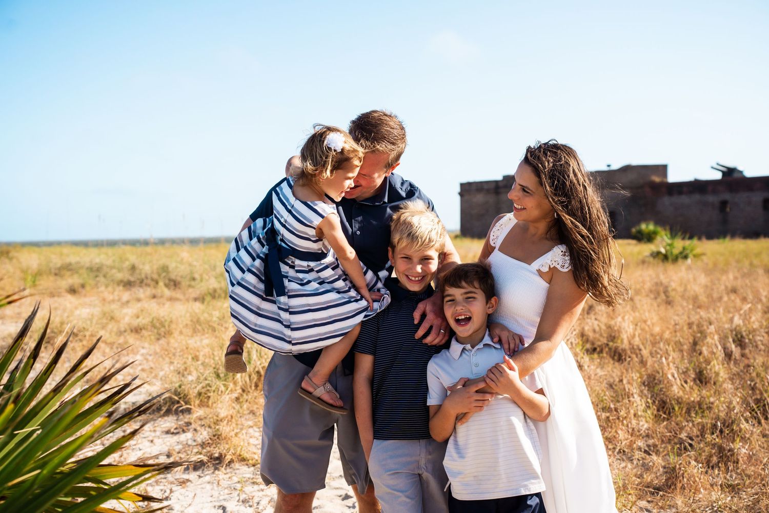 Family embracing and laughing together in sunny coastal setting.