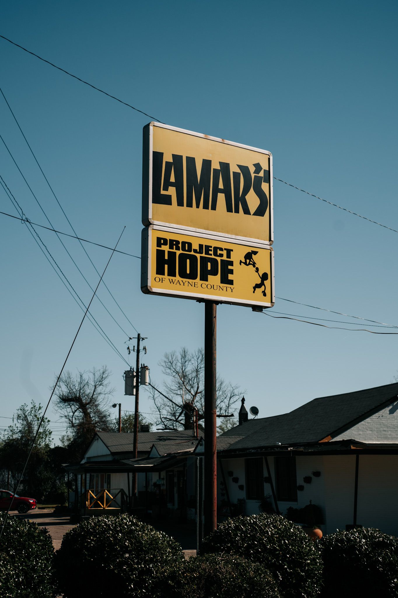 A vintage-style yellow and black sign for Lamar's and Project Hope stands tall against a clear blue sky with power lines.