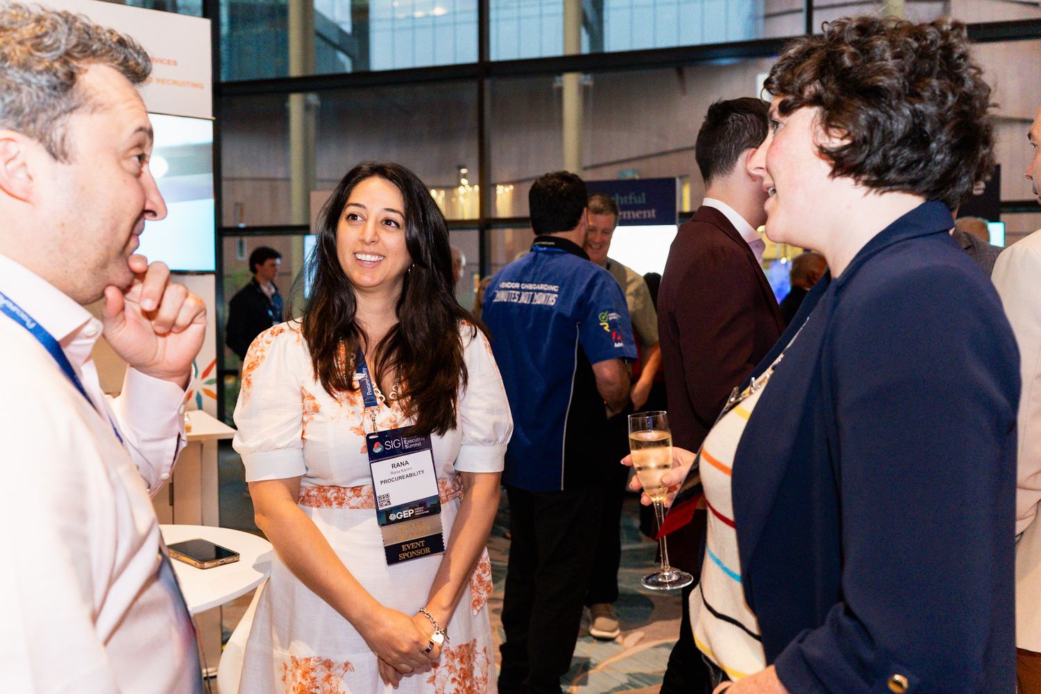 Three professionals networking and conversing at a conference event with name badges.