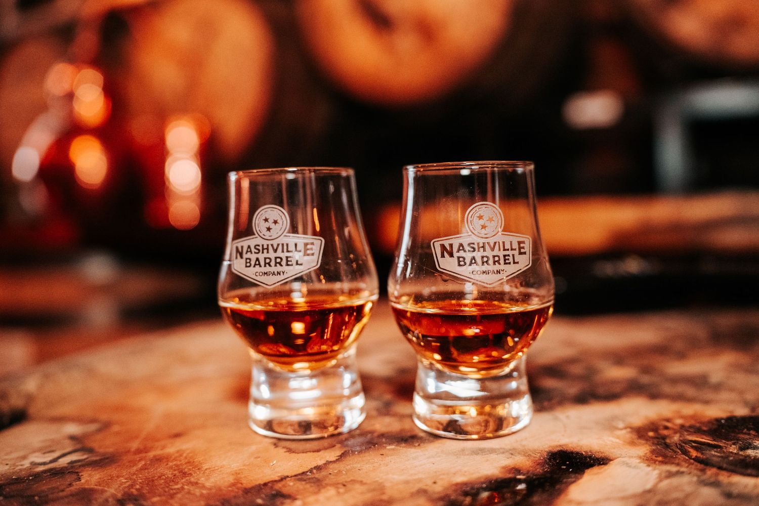 Two Nashville Barrel Co. whiskey tasting glasses filled with amber bourbon sit on a rustic wooden surface.