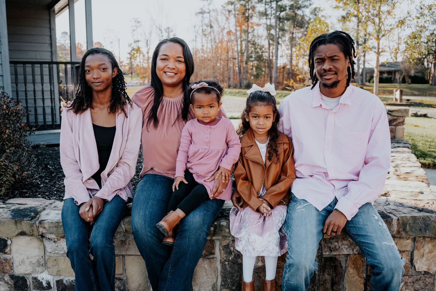 Family of five in coordinating pink and neutral outfits sitting on stone wall.
