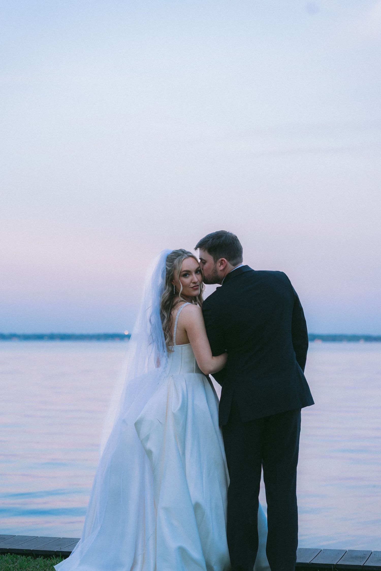 A romantic wedding couple shares intimate moments at sunset on a waterfront dock.