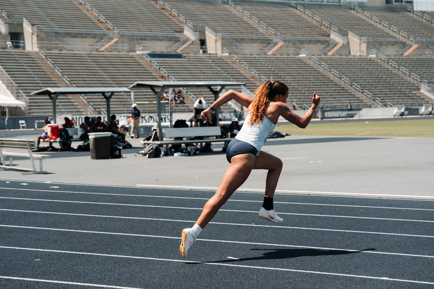 Runner sprinting on outdoor track in mid-stride motion with golf carts visible in background at stadium.