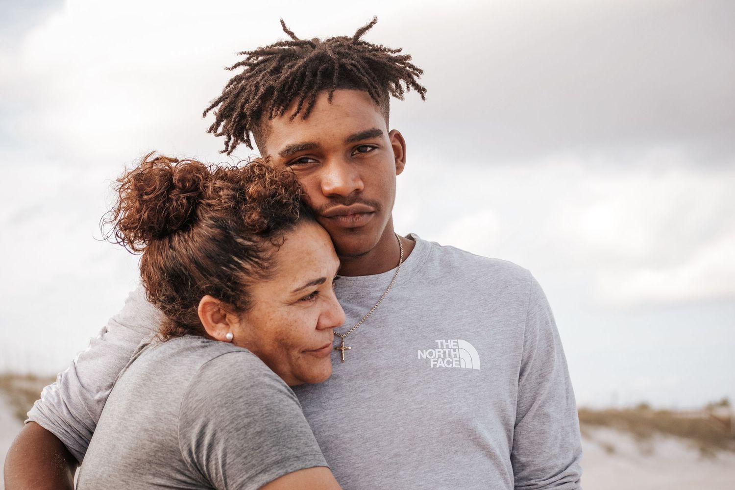 Couple in grey shirts share an intimate moment against cloudy sky.